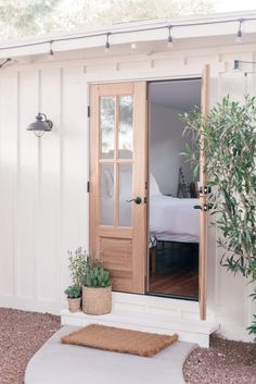 a white shed with a bed and potted plants in front of the door that is open