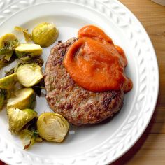 a white plate topped with a hamburger covered in sauce and brussel sprouts