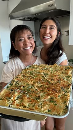 two women are holding up a large casserole