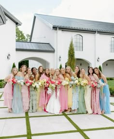 a group of women standing next to each other in front of a white building holding bouquets