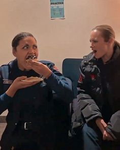 two women eating food while sitting down on the couch in front of a man who is wearing an officer's uniform