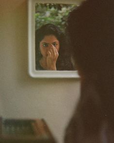 a woman looking at herself in the mirror with her hand to her face and holding her nose