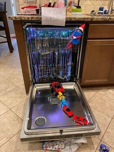 an open dishwasher with toy cars in it on the floor next to a counter