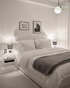 a bedroom with white bedding and pictures on the wall above it, along with two nightstands