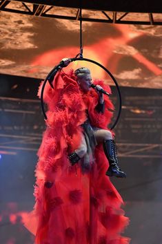 a woman in a red dress is hanging from a hoop with her hands on her hips