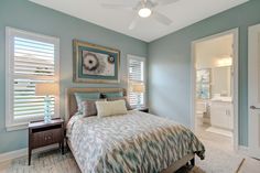 a bed sitting in a bedroom next to two windows with shutters on each side