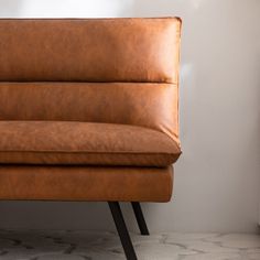 a brown leather couch sitting on top of a white floor next to a lamp and wall