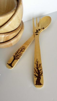 two wooden spoons with trees carved on them next to a bowl and other wood utensils