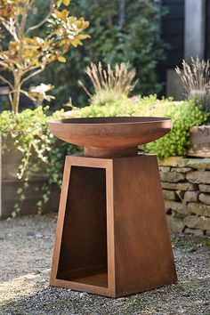 a large wooden bowl sitting on top of a stone slab in front of a garden