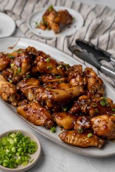 chicken wings with sauce and green onions on a white platter next to silverware