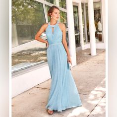 a woman in a long blue dress standing on the sidewalk