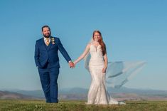 a bride and groom holding hands while standing in a field