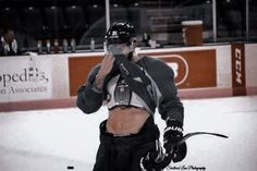 an ice hockey player is standing on the ice talking on his cell phone while holding up his helmet