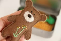 a hand holding a small brown teddy bear with flowers on it's chest and eyes