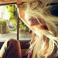 a woman sitting in the back seat of a car with her hair blowing in the wind