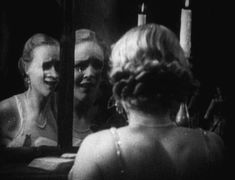 a woman looking at herself in the mirror with candles on her face and another woman's reflection