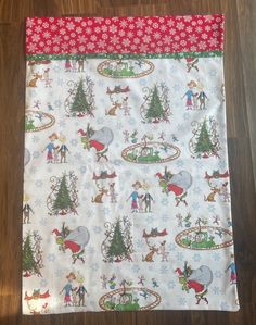 a christmas themed table cloth with people and trees on it, sitting on a wooden floor