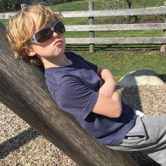 a young boy wearing sunglasses sitting on top of a wooden bench next to a fence