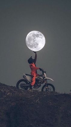 a person on a dirt bike with the moon in the sky behind them and one hand up above their head