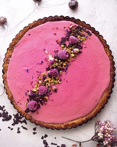 a pie with pink frosting and purple flowers on the top is surrounded by confetti sprinkles