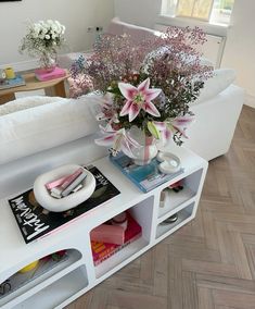 a vase with flowers sitting on top of a book shelf next to a couch and coffee table