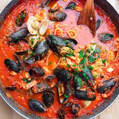 a pan filled with pasta and mussels on top of a wooden table