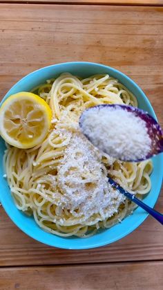 a blue bowl filled with pasta and lemons on top of a wooden table next to a spoon