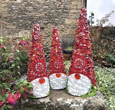 three red and white christmas trees sitting on top of a stone wall next to flowers