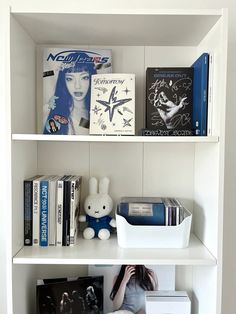 a white book shelf filled with books and other items next to a stuffed animal on top of it