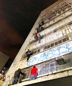 people climbing up the side of a tall building with graffiti on it's sides