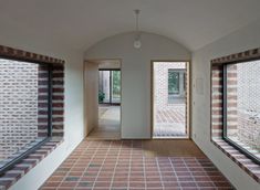 an empty room with brick walls and large windows on either side of the door, leading to another room