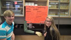 two people standing next to each other in front of a counter with writing on it