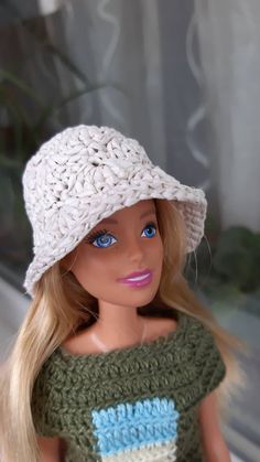 a barbie doll wearing a crocheted hat and green shirt with blue eyes in front of a window