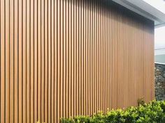 the side of a building with wooden slats on it's sides and bushes in front