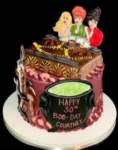 a birthday cake decorated with two women sitting on top of a book and caulder