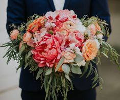 a man in a suit holding a bouquet of flowers with greenery on the side