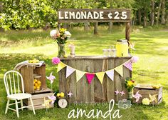 a lemonade stand is set up in the grass with flowers, lemons and bunting