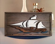 a wooden box with a sailboat on it and two bottles in the back ground