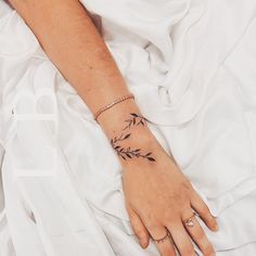 a woman's hand with a small tattoo on her left wrist, resting on a white sheet