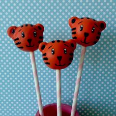 three orange cake pops with black and white tiger faces on them, sitting in a pink cup