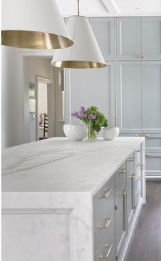 a white kitchen with marble counter tops and gold accents on the ceiling, along with two brass pendant lights