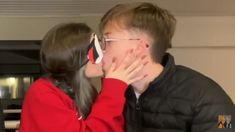 a young man and woman kissing each other in front of a tv screen with their hands covering their mouths