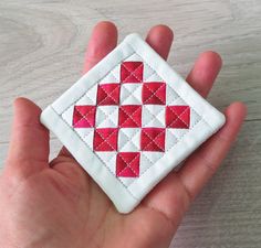 a hand holding a small red and white patchwork square