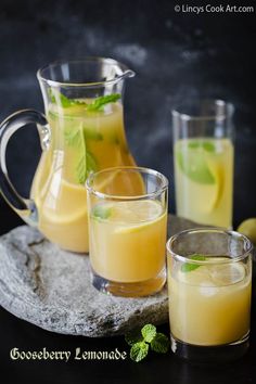 three glasses filled with lemonade sitting on top of a stone slab next to two pitchers