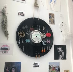 a black clock hanging from the side of a white wall covered in pictures and jewelry