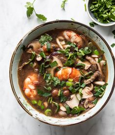 a bowl of soup with shrimp, mushrooms and greens on the table next to it