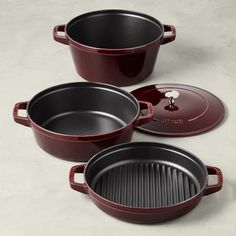 three red cast iron pots and pans on a white table with a black lid