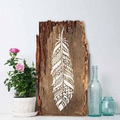 a wooden sign with a white feather on it next to some vases and flowers