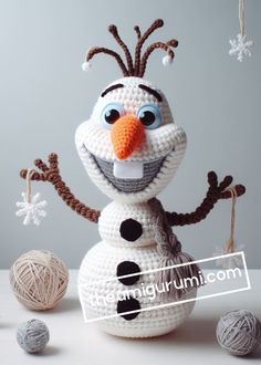 a crocheted snowman with two balls of yarn around it and one ball of yarn in the foreground