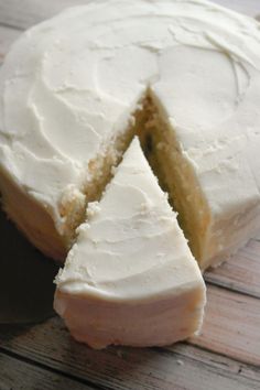 a cake with white frosting sitting on top of a wooden table next to a slice cut from it